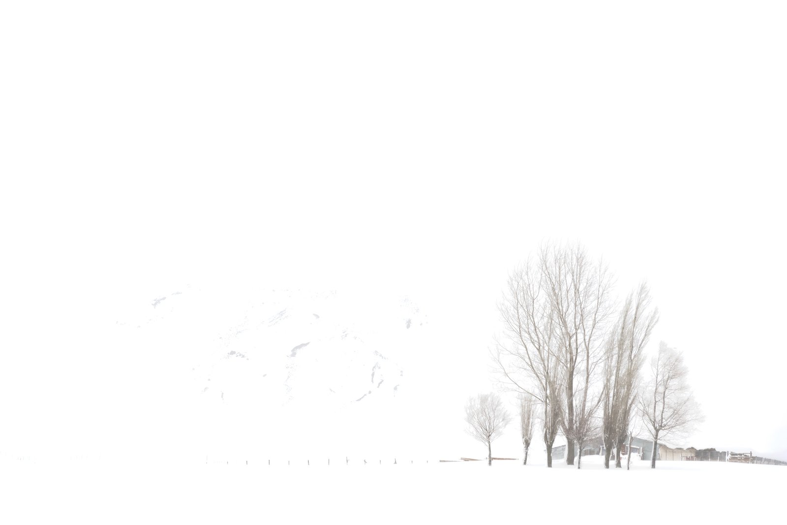 minimal winter landscape with fading trees and distant structure in snow – fine art photography from the Winter Silence series by Aris Dimakopoulos